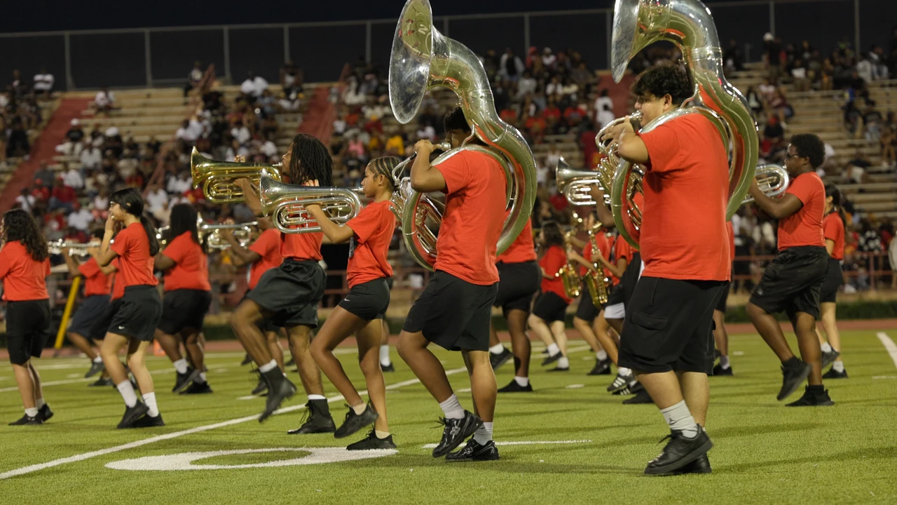 Madison's brass section marching across the field, with spectators in the stands behind them.