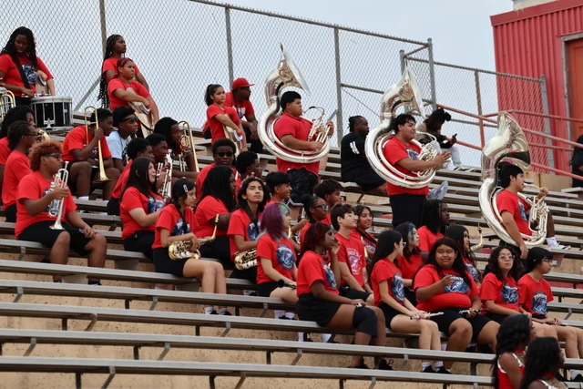 Musicians in red shirts with brass instruments gathered on the stadium bleachers.
