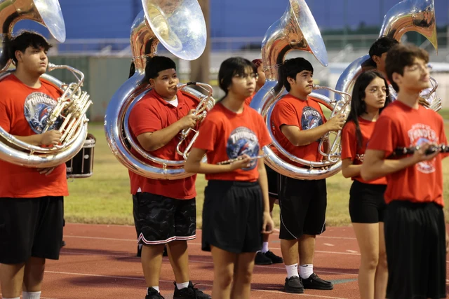 Band members in red shirts holding silver sousaphones and smaller brass instruments beside the track.