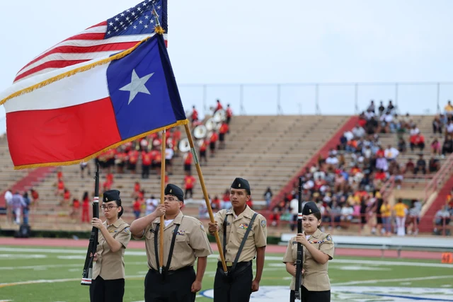 The color guard carrying the United States and Texas flags in front of the stadium stands.