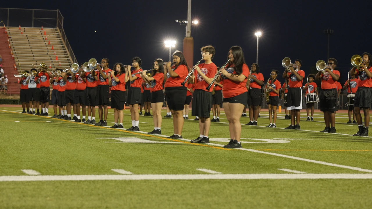 The full marching band performing in rows across the field under the stadium lights.